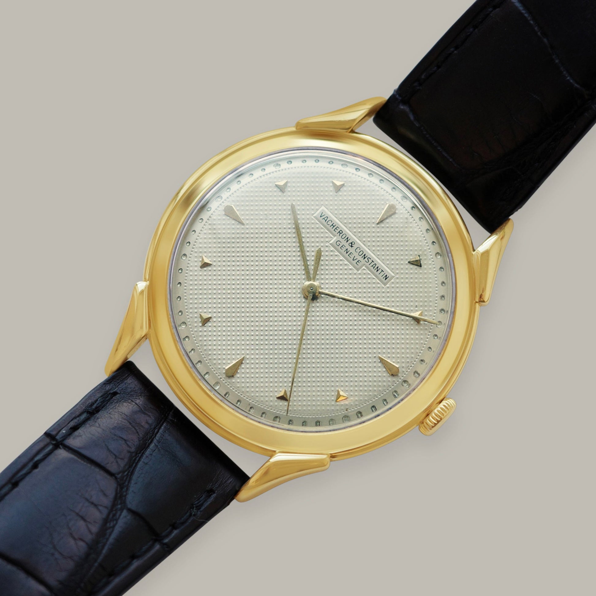 Gold wristwatch with black leather strap on a gray background